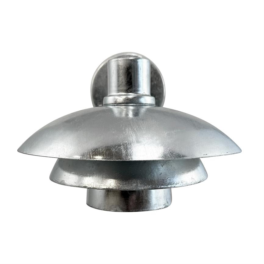Sølvfarvet metalvæglampe med tre lagdelte, skålformede skærme; monteret på en rund vægplade; fotograferet mod ensartet hvid baggrund, studiobelysning fremhæver den matte metalglans.