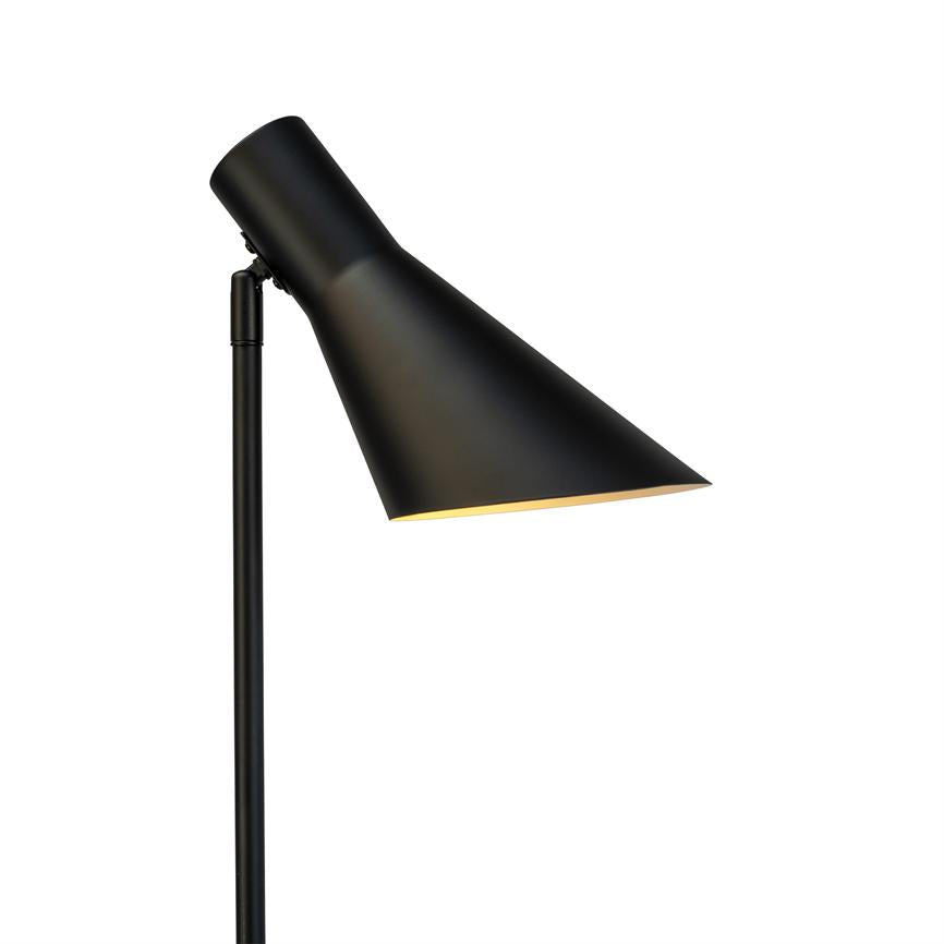 Sort standlampe med konisk skærm, vippet skråt og udsender blødt, varmt lys nedad; enkel sort stang mod en neutral hvid baggrund.