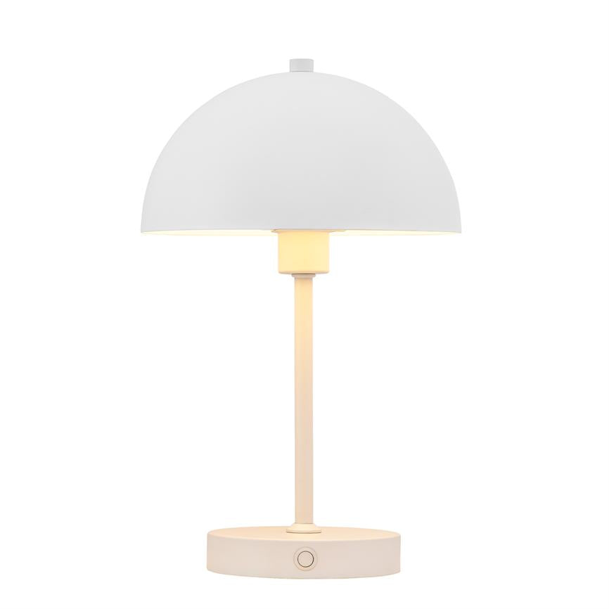 Bordlampe med halvkuppelformet skærm, udsender blødt varmt lys, monteret på slank stang og rund base, står centralt mod ensartet hvid baggrund.