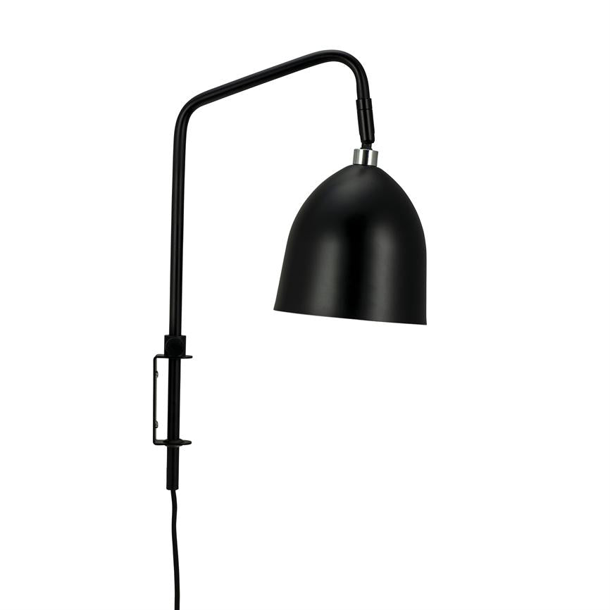 Sort metal væglampe hænger fra en buet arm; den klokkeformede skærm er vinklet nedad; armens lodrette stang har klemmebeslag og sort ledning mod hvid baggrund.