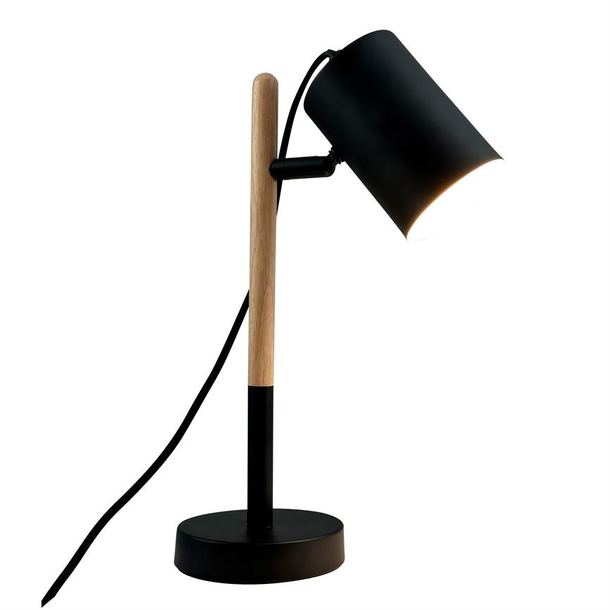 Skrivebordslampe står tændt, skærm vinklet nedad; træstang og rund sort metalbase holder lampen; sort ledning hænger ned foran hvid baggrund.