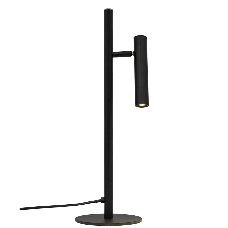 En slank, sort skrivebordslampe med vertikal stang og cylindrisk lampehoved, der peger nedad og afgiver svagt lys; står på rund fod mod hvid baggrund med synlig ledning.