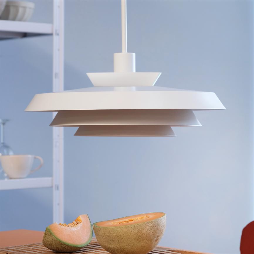 Objekt: Hvid, lagdelt pendellampe. Handling: Hænger roligt fra loftet. Kontekst: Lys, minimalistisk køkken/spisebord med halveret cantaloupe-melon på bordet og hylde med kop i baggrunden.
