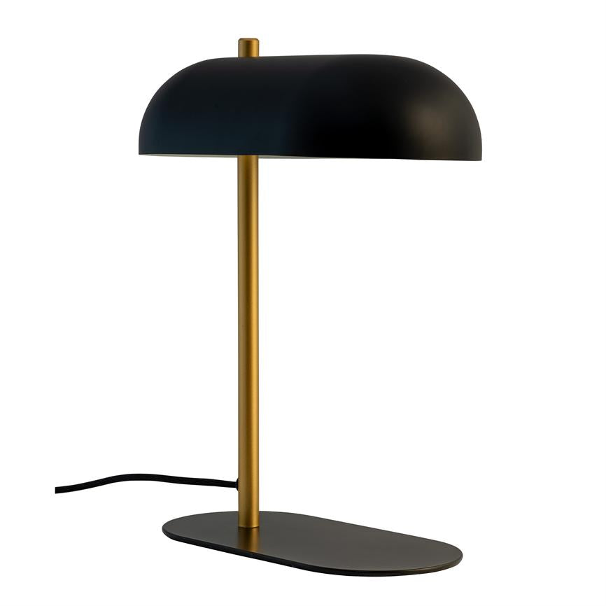 Sort og messing bordlampe står på en flad oval sort fod; en smal messingstang fører op til en halvkugleformet sort skærm, foran en hvid, neutral baggrund.
