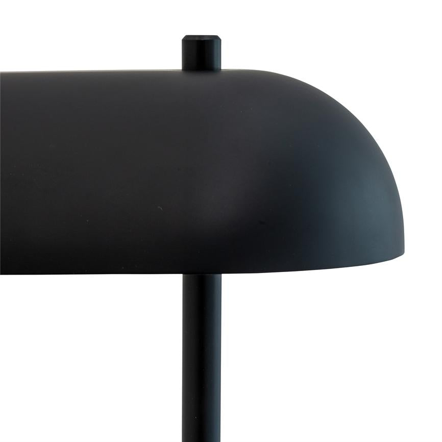 En sort, buet bordlampe med lille topknap hviler på en smal lodret søjle foran en ensartet hvid baggrund.