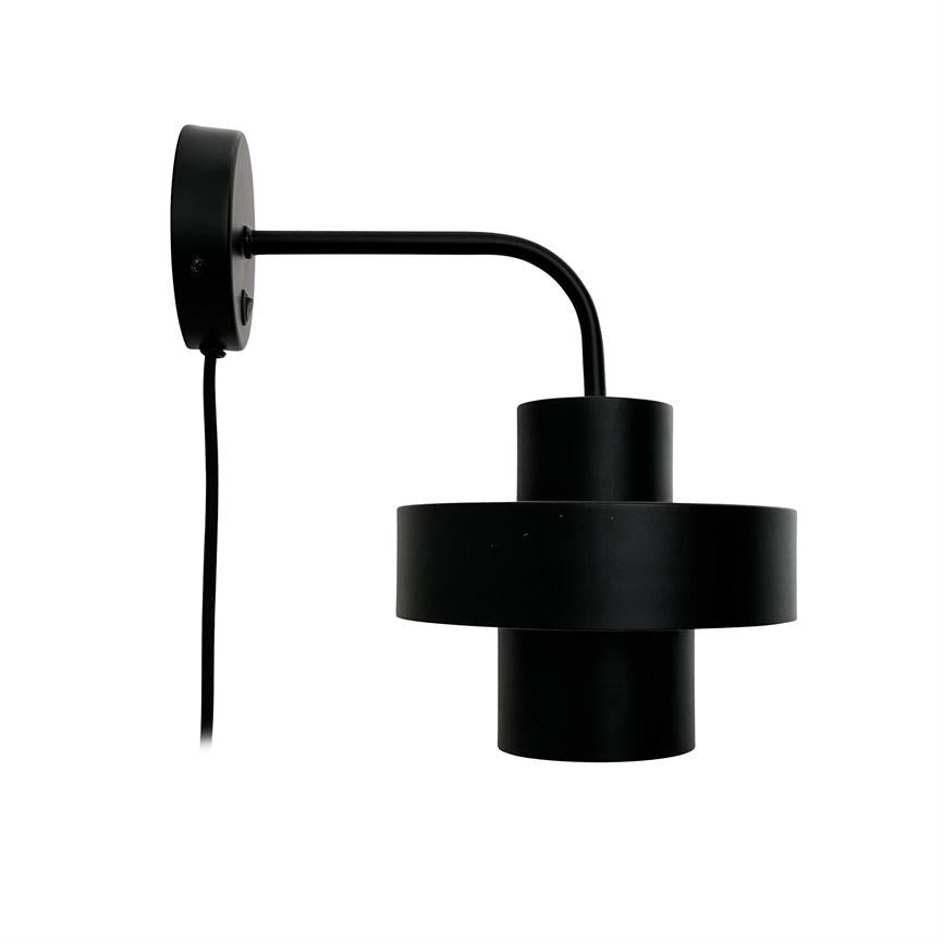 Vægmonteret sort metal lampe med cylindrisk, to-lags skærm hænger fra en buet arm på en neutral hvid baggrund.