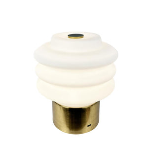 Bordlampe med ribbet hvid opalglaskuppel, udsender blødt varmt lys; hviler på cylindrisk børstet messingfod med lille USB-port, mod neutral hvid baggrund.