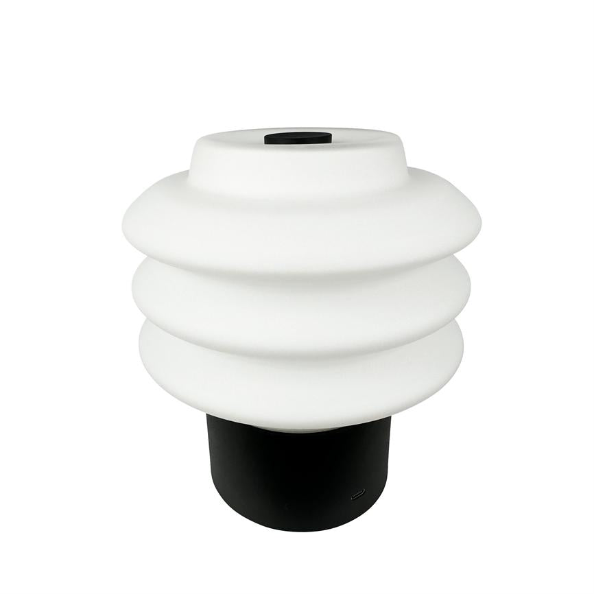 Bordlampe med lagdelt, bølget hvid skærm, hviler på en sort cylindrisk base på en ensfarvet hvid baggrund.