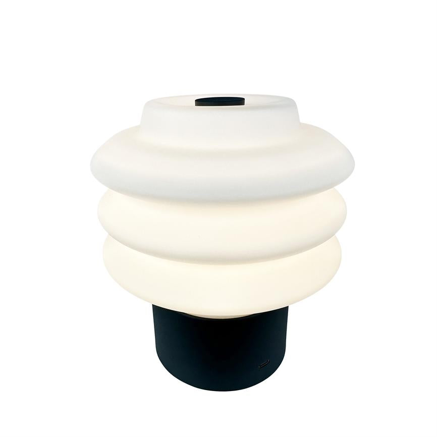 Bordlampe med hvid, bølget skærm i tre lag, der lyser blødt; sort cylinderfod under skærmen, mod en neutral hvid baggrund.
