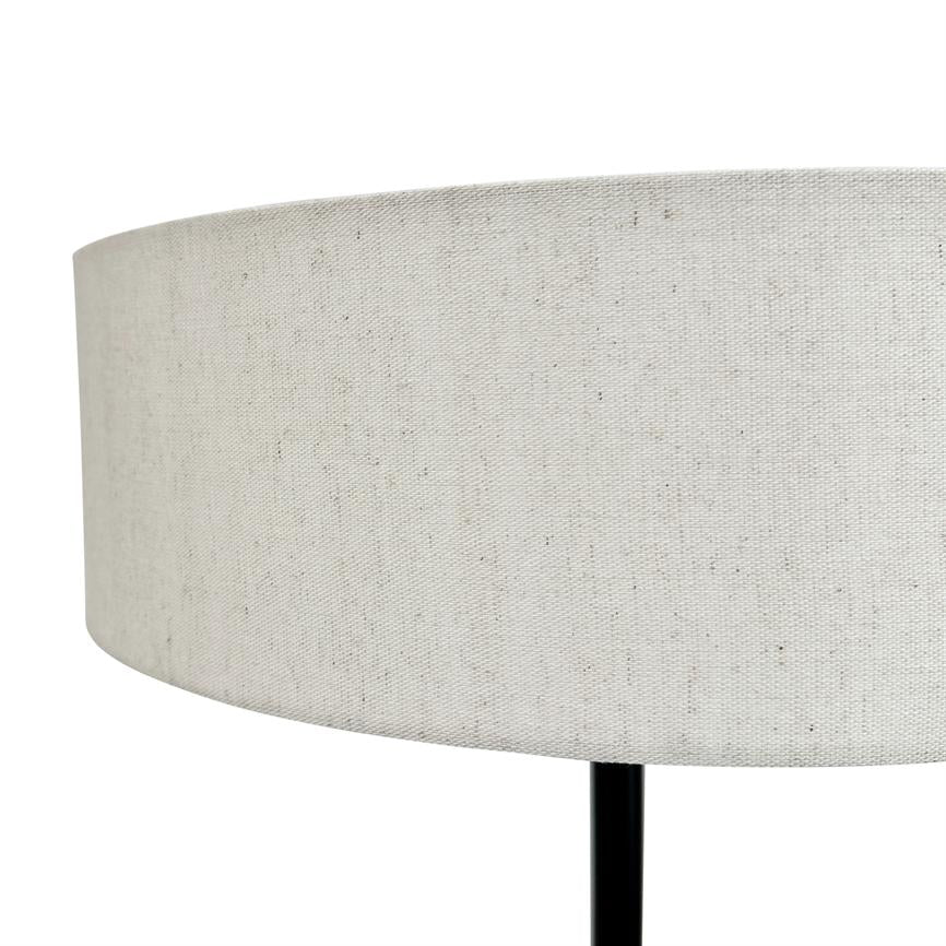 Lampskærm i lys, meleret stof hviler på en slank sort lampefod; nærbillede af en cylindrisk form mod en ensartet hvid baggrund.
