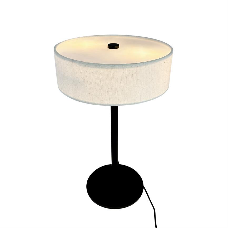 Bordlampe med rund, hvid stofskærm, der udsender varmt, blødt lys; tynd sort stang og rundt sort fod, med synlig sort netledning, fotograferet på hvid baggrund.
