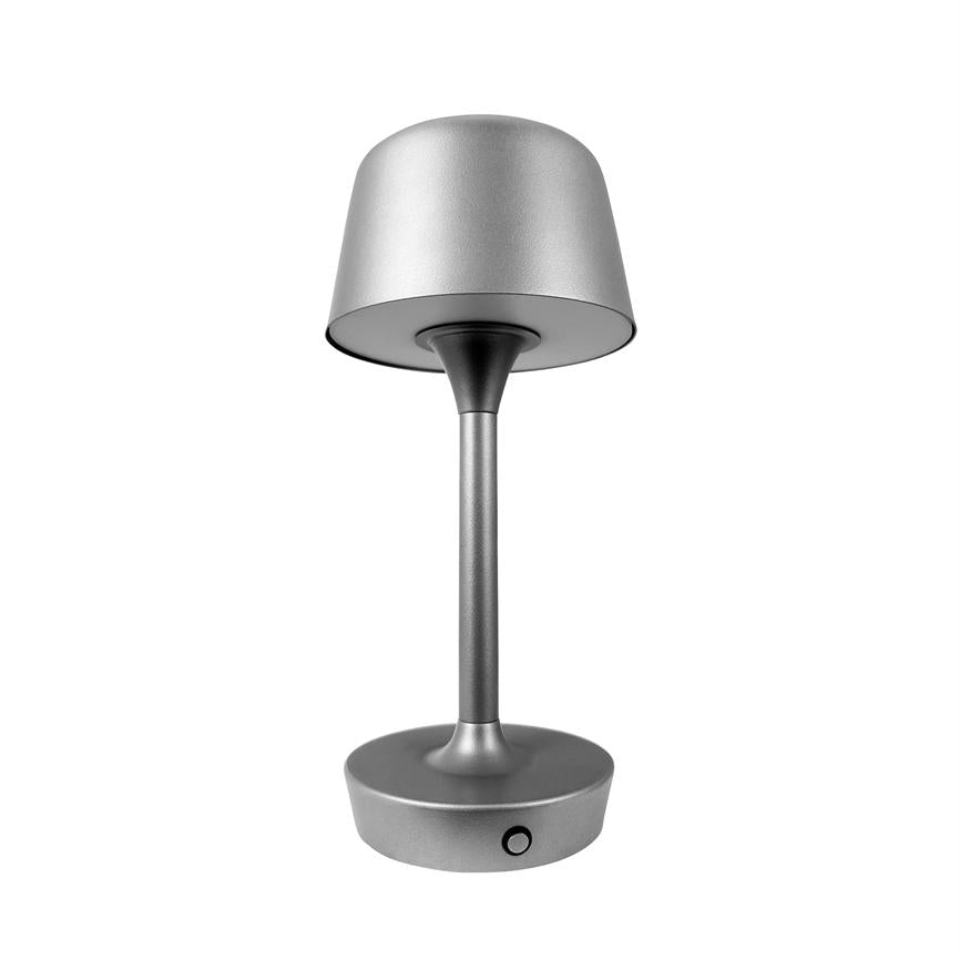 Bordlampe i sølvmetal står på hvid baggrund; enkel cylindrisk fod, slank skaft, kuppelformet skærm og rund base med lille tænd/sluk-knap.
