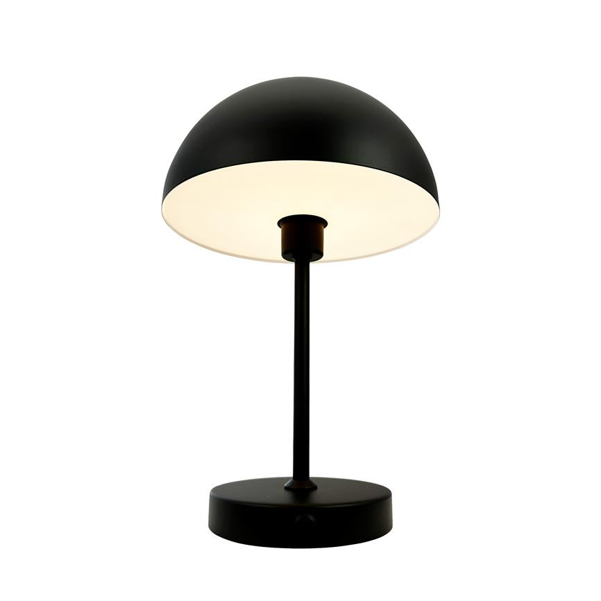 Bordlampe med sort kuppelskærm lyser blødt nedad; monteret på en slank sort stang og rundt fodstykke, isoleret mod en neutral hvid baggrund.