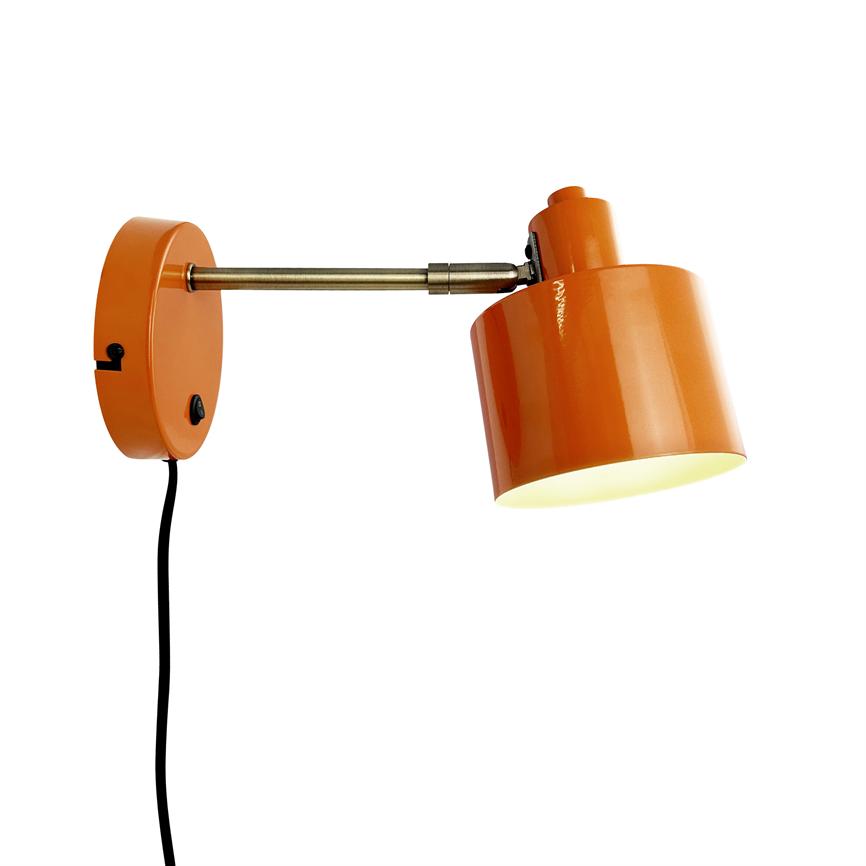 En orange væglampe monteret på en drejet metalarm, lyser nedad; rund vægplade og sort ledning synlig mod en neutral hvid baggrund.