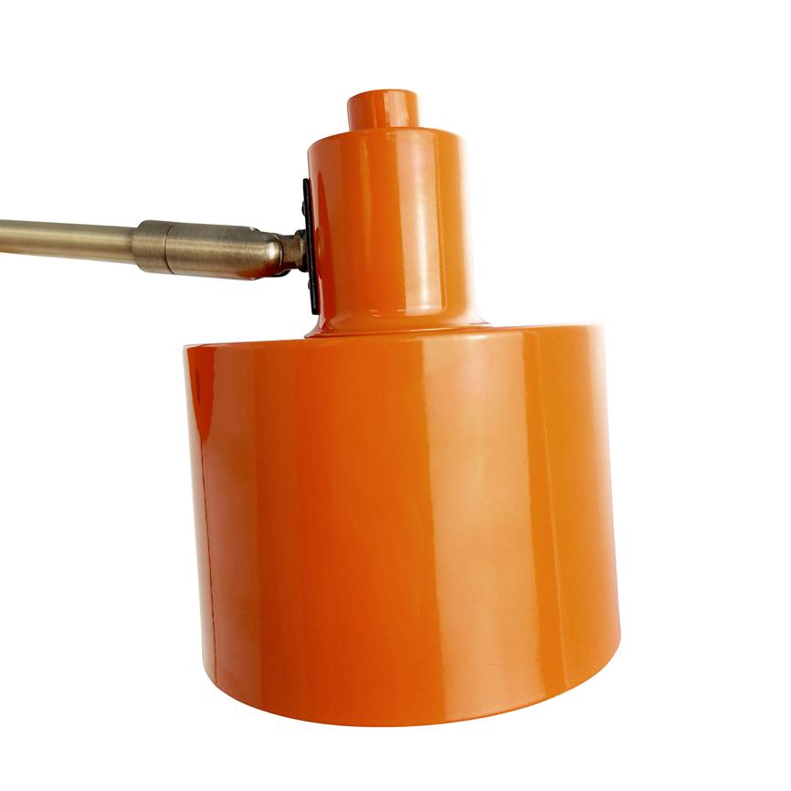 Orange cylindrisk lampehoved sidder vinklet fast på en messingarm, med reflekterende lakoverflade og fremhævet mod en ren, hvid baggrund.