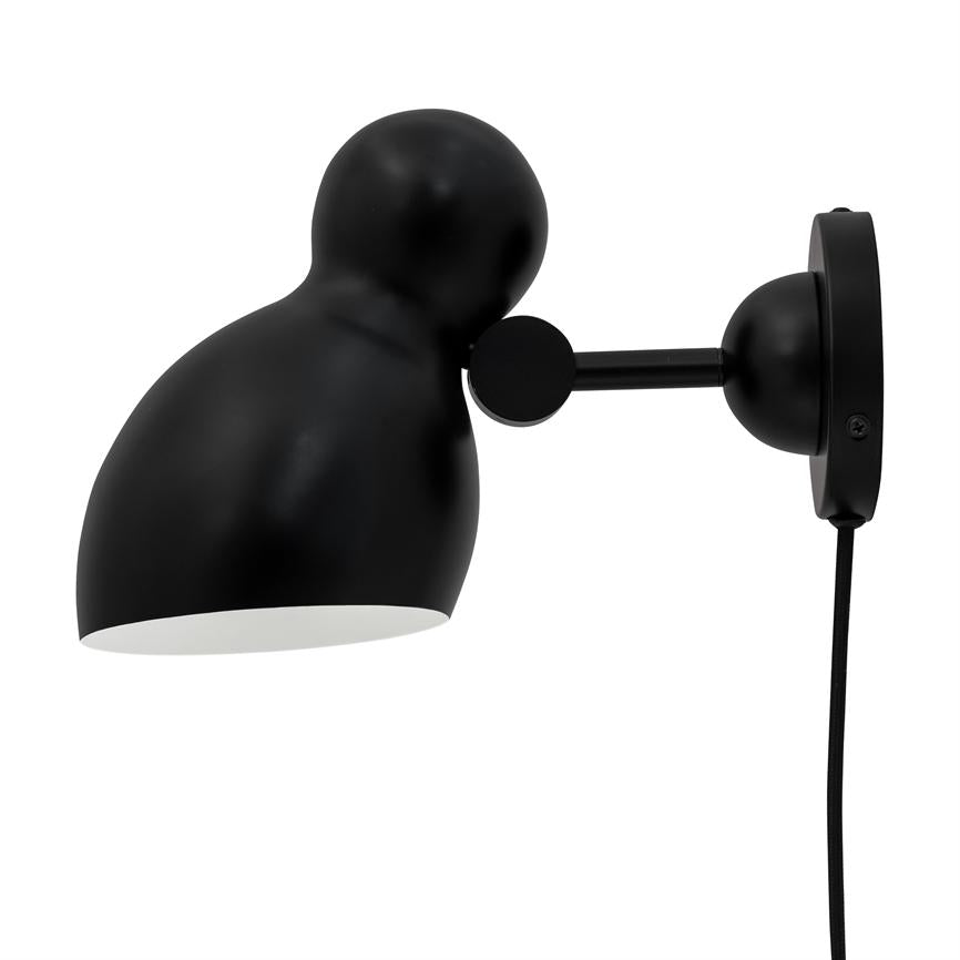 Sort væglampe med justerbart led og rund vægplade; lampeskærm peger nedad, tekstilkabel hænger lodret mod højre på en hvid baggrund.