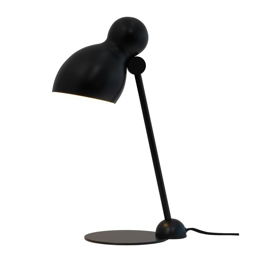 Sort skrivebordslampe hælder fremad og kaster lys nedad; slank skrå arm og rund skærm monteret på flad, cirkulær fod mod en ren hvid baggrund.