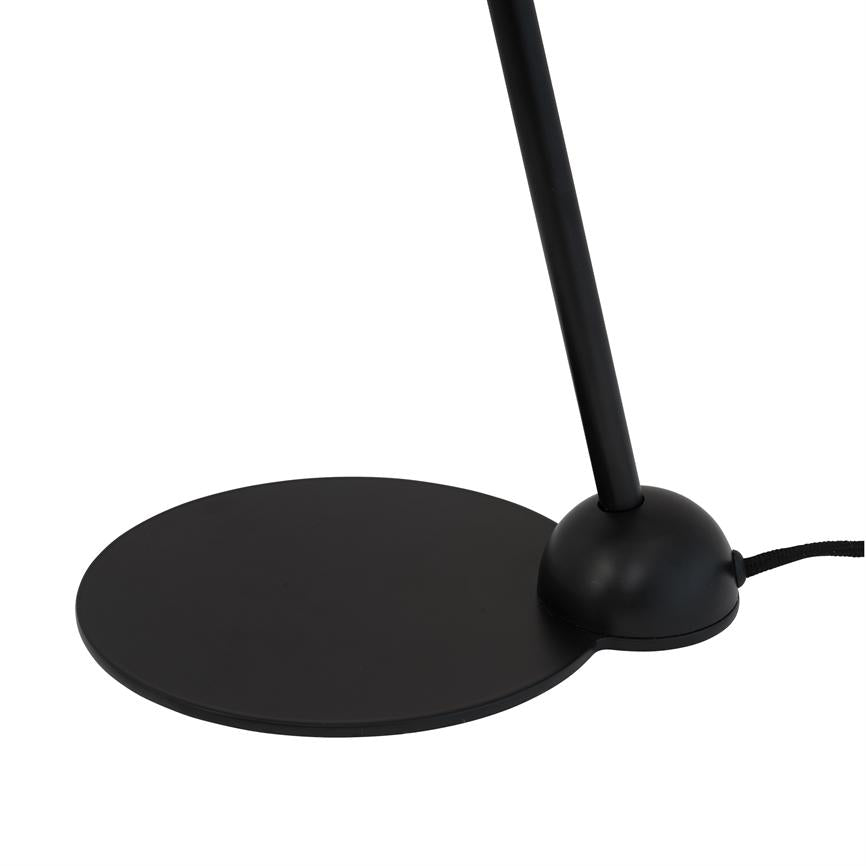Sort bordlampe med flad, rund fod og afrundet sokkel; en slank stang hælder opad fra soklen. Står alene mod en ensartet, hvid baggrund.