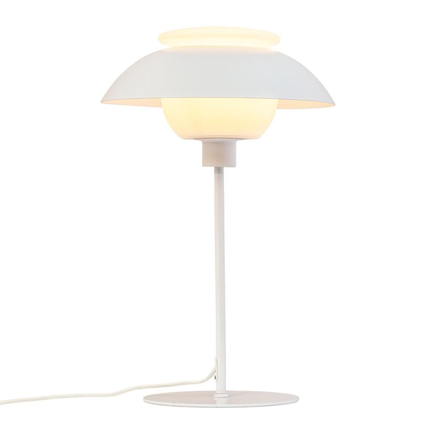 En hvid bordlampe med lagdelt kuppel udstråler varmt, blødt lys på et slankt stativ med rund fod og synlig ledning mod en ensartet hvid baggrund.