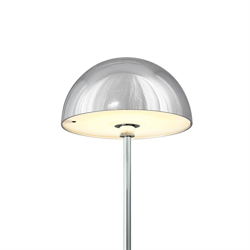 Krom gulvlampe udsender blødt, varmt lys under en halvkugleformet skærm; slank metalstang og reflekterende kromoverflade mod ensartet hvid baggrund.