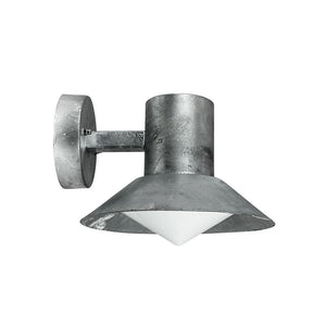 Væglampe: rå metalcylinder med bred, kegleformet skærm og hvid, pyramideformet diffuser; monteret på rundt vægbeslag via kort arm, vender nedad mod en neutral hvid baggrund.