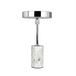 Bordlampe står lodret med rund, blank kromskærm og slank stang; den hviler på en cylinderformet hvidgrå marmorbase mod en ensartet hvid baggrund.