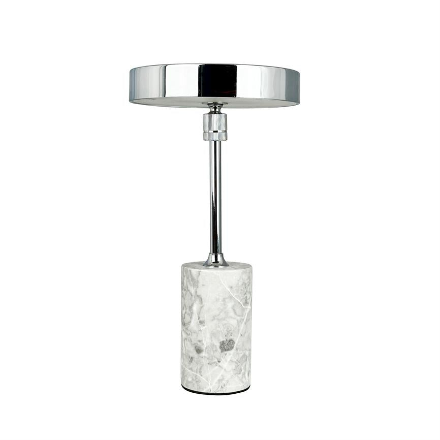 Bordlampe står lodret med rund, blank kromskærm og slank stang; den hviler på en cylinderformet hvidgrå marmorbase mod en ensartet hvid baggrund.