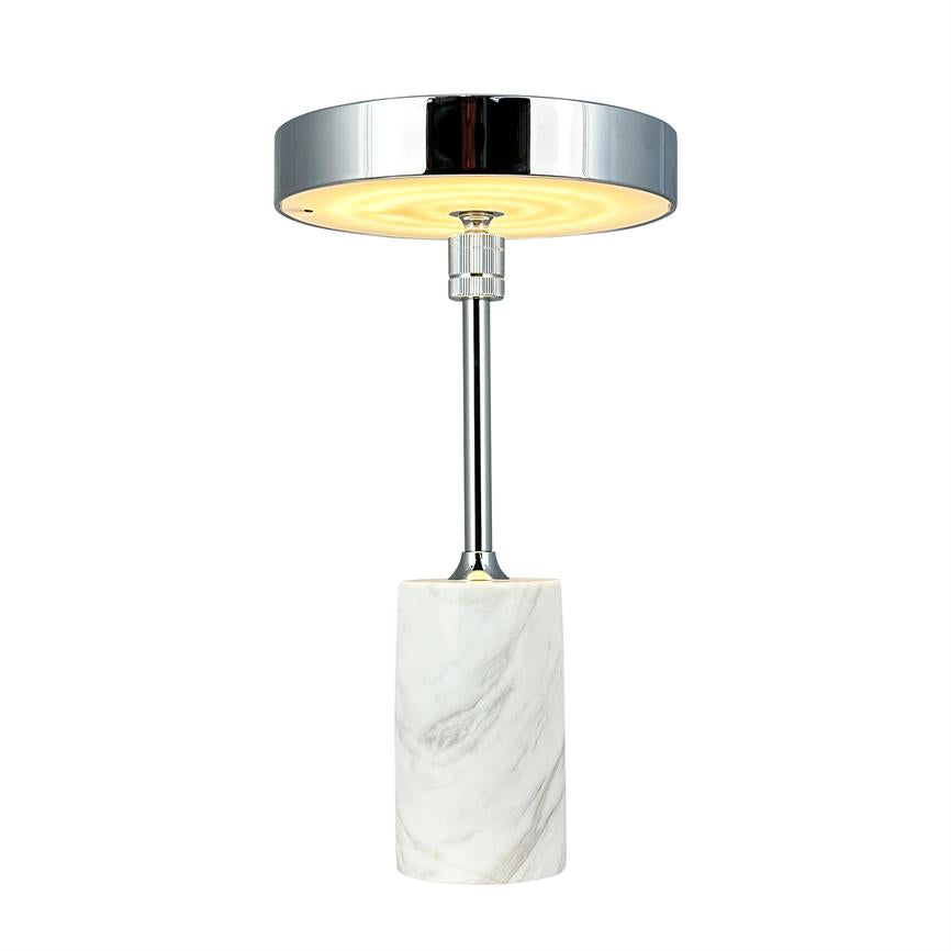 Lampe udsender varmt, diffust lys fra en krom cirkulær skærm, hævet på en slank kromstang over en cylindrisk hvidmarmorfod på neutral hvid baggrund.