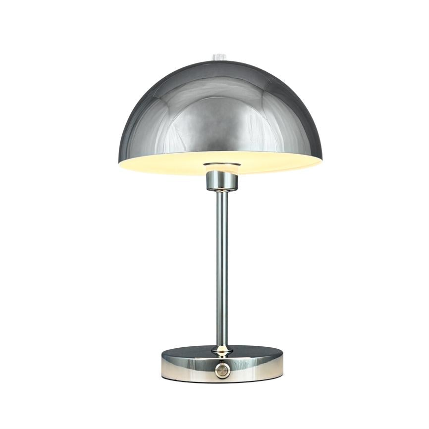 En krom bordlampe med halvkugleformet skærm lyser varmt nedad; slank stang og rund fod med trykknap står på hvid baggrund.