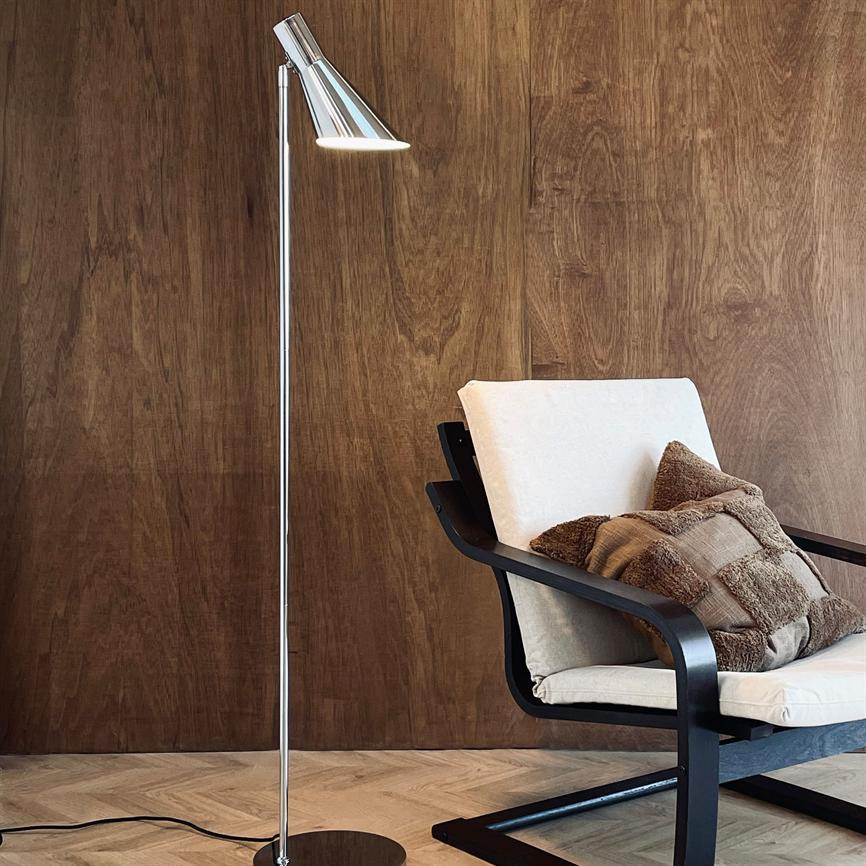 Gulvlampe står tændt ved siden af en polstret lænestol med beige hynde og brune puder, foran en varm træbeklædt væg og lyst sildebensparketgulv.