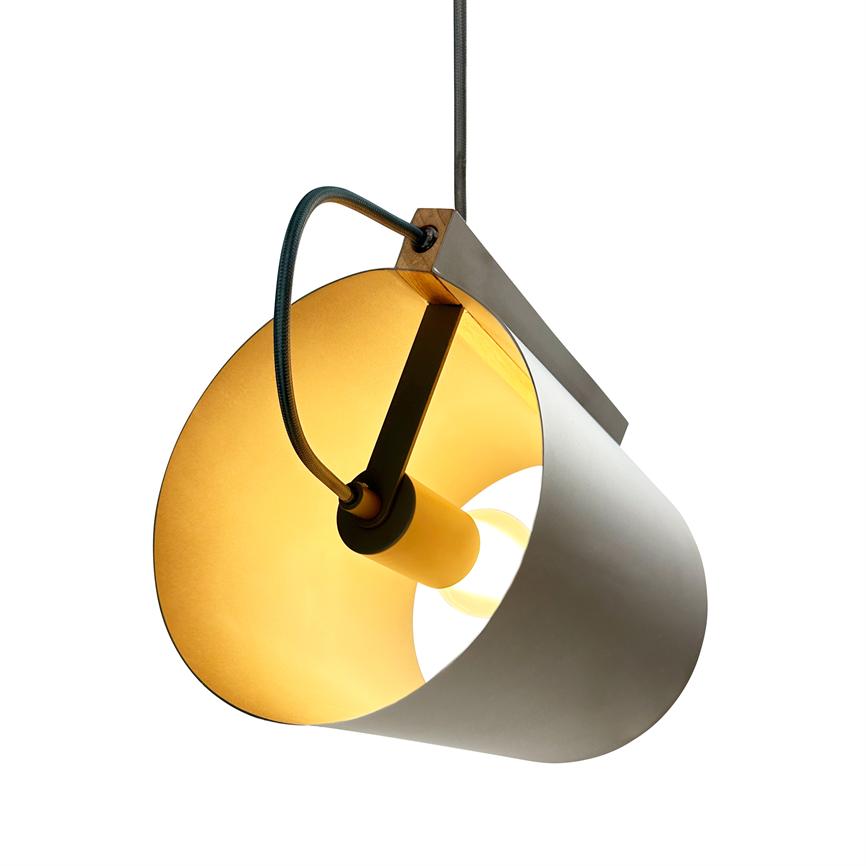 En cylindrisk loftslampe oplyser varmt; den hænger i en stofledning, skærmens inderside er gylden, og lampen er monteret på en skrå metalarm foran en hvid baggrund.
