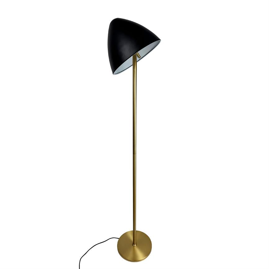 Gulvlampe med sort skrånende skærm står på høj, slank messingstang over rund messingfod; en løs sort ledning ligger på neutral hvid baggrund.