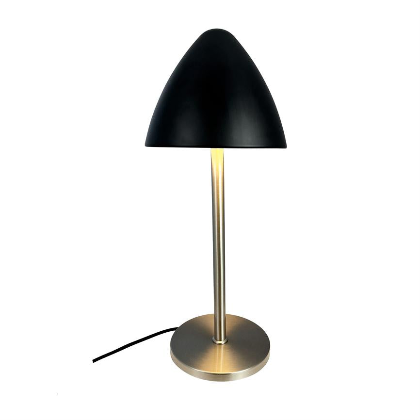 Bordlampe kaster varmt lys nedad; slank børstet metalstang og rund fod står på hvid baggrund, med sort kuppel og synlig sort ledning.