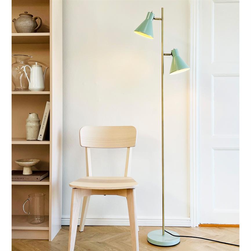 En lys træstol står stille foran en hvid væg, ved siden af en tændt mintgrøn gulvlampe og en hylde med keramiske genstande. 
 Tekst i billedet: "KINFOLK" (på bogryg).