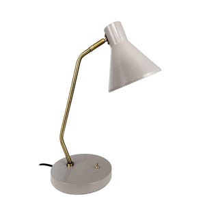 En lysgrå skrivebordslampe peger sin koniske skærm nedad; en buet messingsøjle forbinder skærm og rund grå base på en ens hvid baggrund.