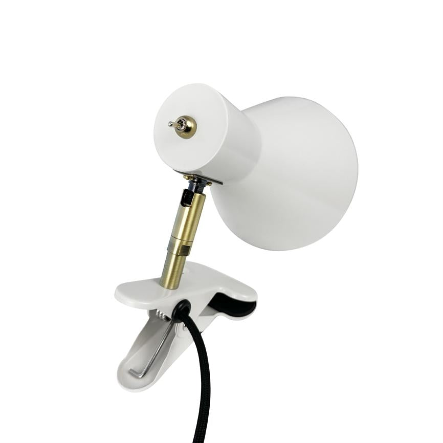 En hvid klemmebordslampe klemmer sig fast, vipper sin koniske skærm opad via et messingfarvet led/ledningsstykke; en sort stofledning hænger ned foran en neutral hvid baggrund.