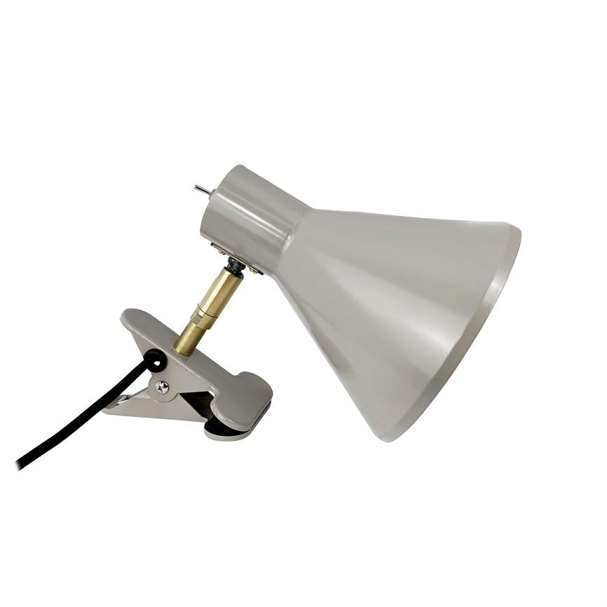 Klipslampe med kegleformet skærm, hælder skråt mod højre og er fastgjort til en metallisk klemme via en justerbar messingled; sort ledning løber ud mod venstre.
