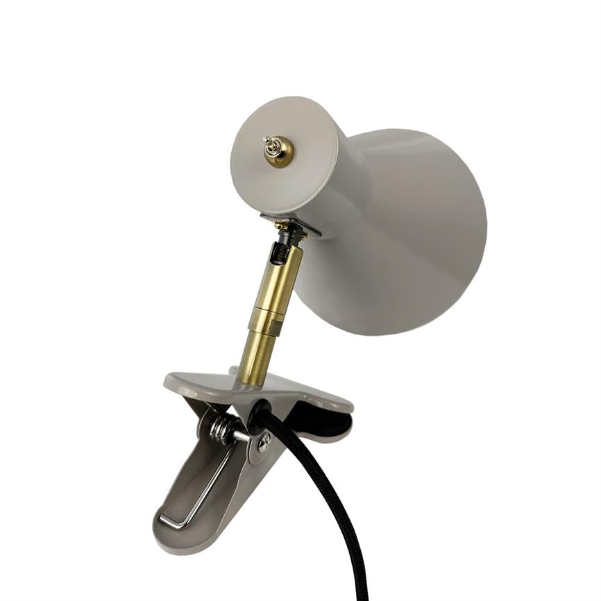 Klemme-lampe med grå skærm, justerbar guldfarvet stang og sort tekstilledning; lampen er vinklet og fastklemmet på en metalclips mod en hvid, neutral baggrund.