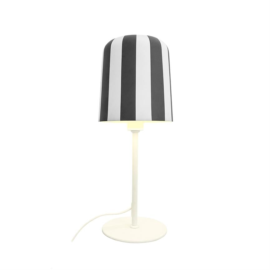Bordlampe står tændt; skærm med sorte og hvide lodrette striber, slank hvid metalstolpe og rund fod på ensartet hvid baggrund.
