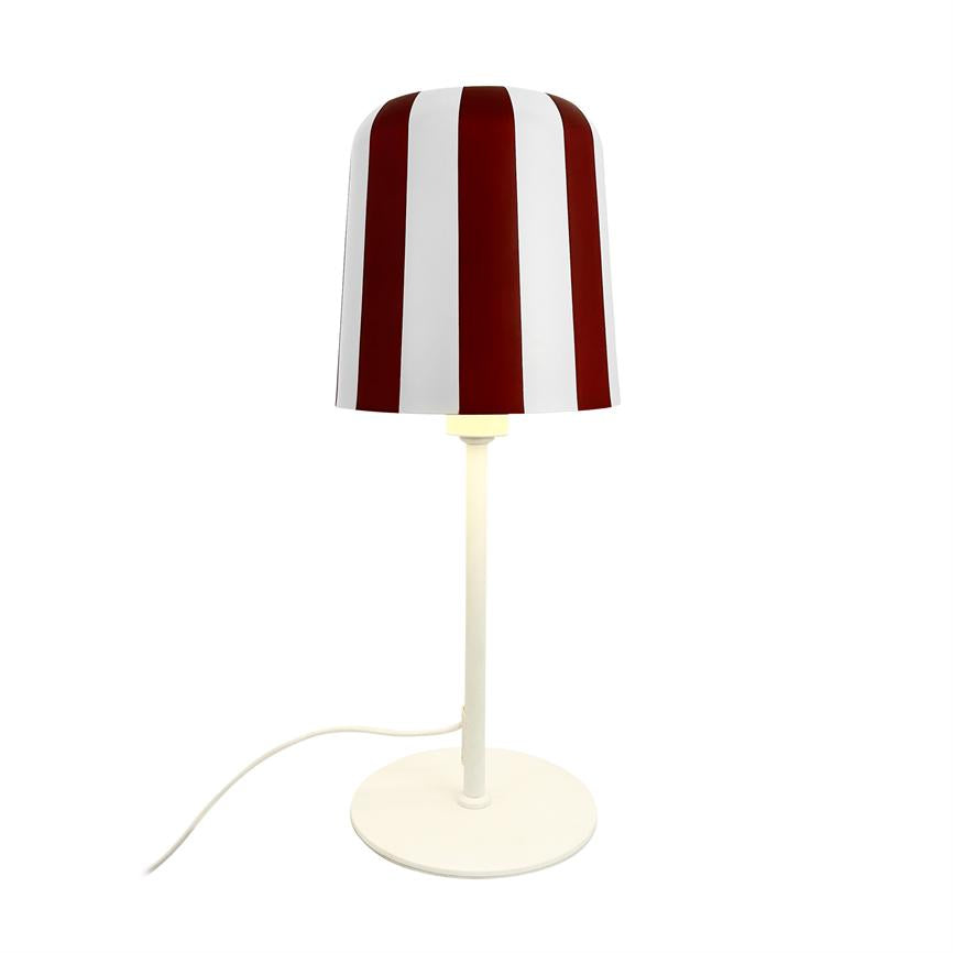 Bordlampe med rød-hvid, lodret stribet skærm lyser svagt; slank hvid stang og rund fod står på hvid baggrund, med hvid ledning der løber ud til venstre.