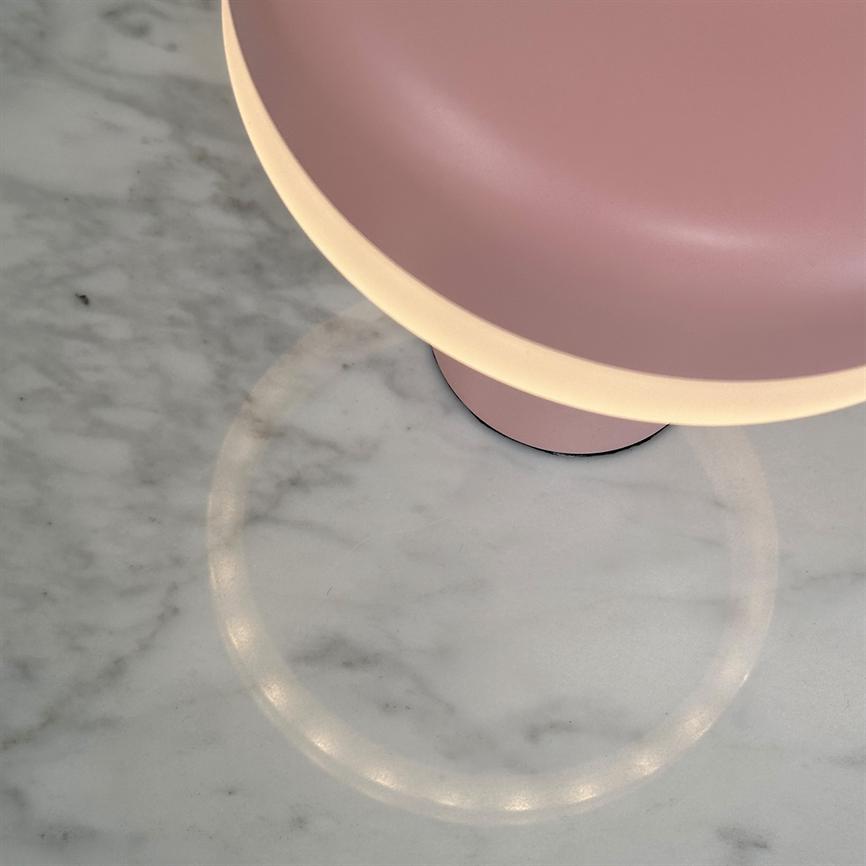 Rosa, skålformet lampe (delvist synlig) kaster en varm, ringformet lysrefleksion på en hvid marmorbordplade med svage årer.