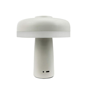 En hvid svampeformet bordlampe står centralt; den har en cylindrisk fod, rund skærm og synlige porte (USB‑C og lille indikatorhul) mod en ensartet hvid baggrund.