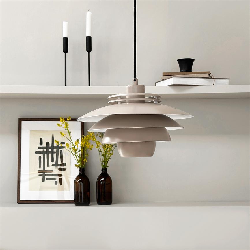 En beige, lagdelt pendellampe hænger over en minimalistisk hylde med to brune glasflasker med gule blomster, en indrammet abstrakt plakat, to sorte lysestager og en lille bogstak.