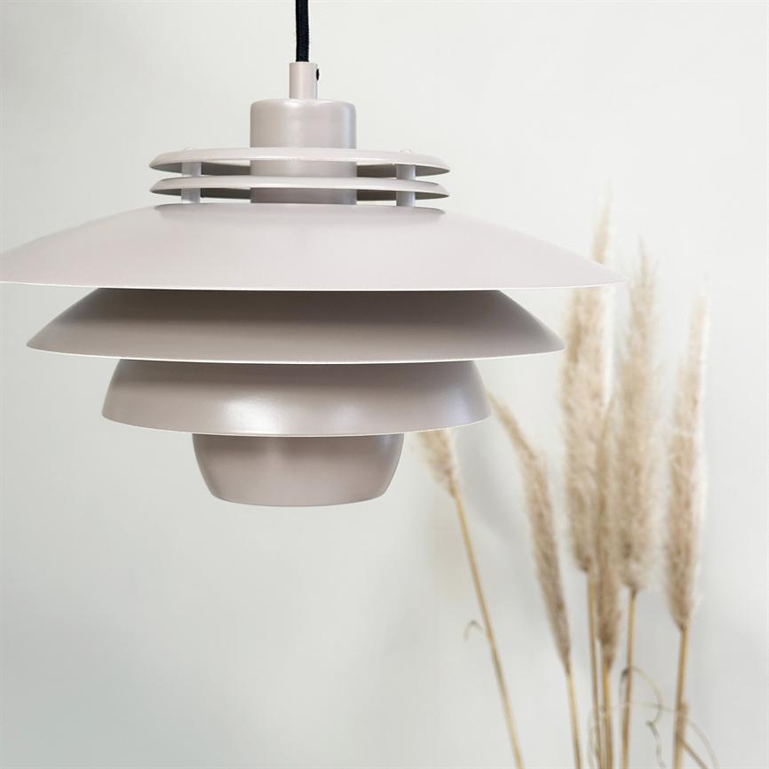 En lagdelt, beige metal hængelampe hænger fra en sort ledning over en lys væg, foran dekorative tørrede pampasgræsser, hvilket skaber et minimalistisk, skandinavisk interiørudtryk.