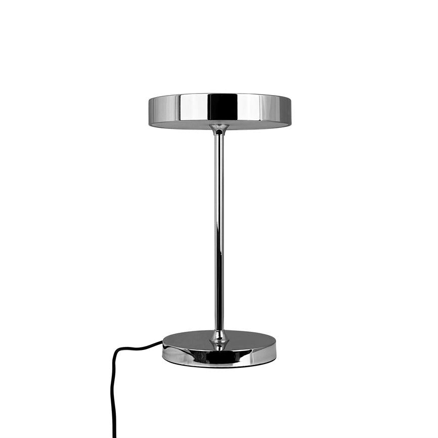 Krom bordlampe hviler med flad, rund skærm på en slank søjle; står på en rund base, og en sort ledning løber ud mod siden mod hvid baggrund.