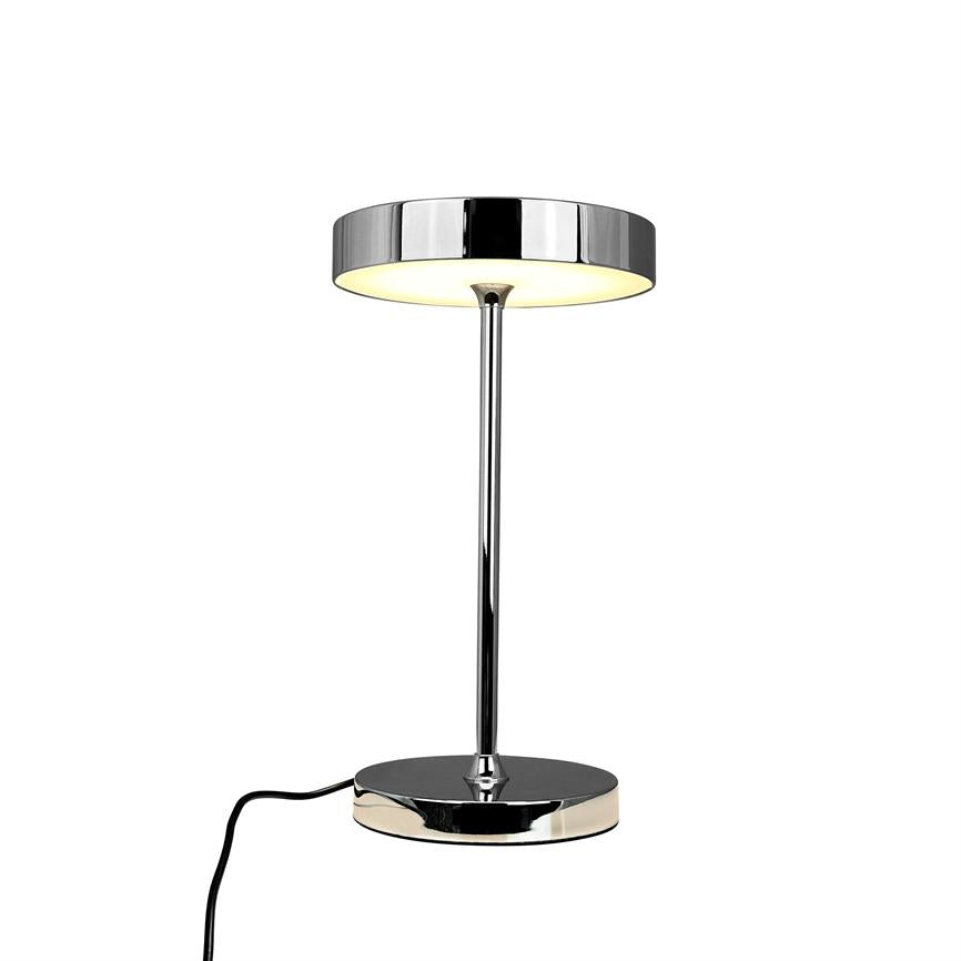 Krom bordlampe med rund skærm lyser blødt nedad, monteret på slank stang og rund fod; sort ledning fører fra basen mod forgrunden på hvid baggrund.