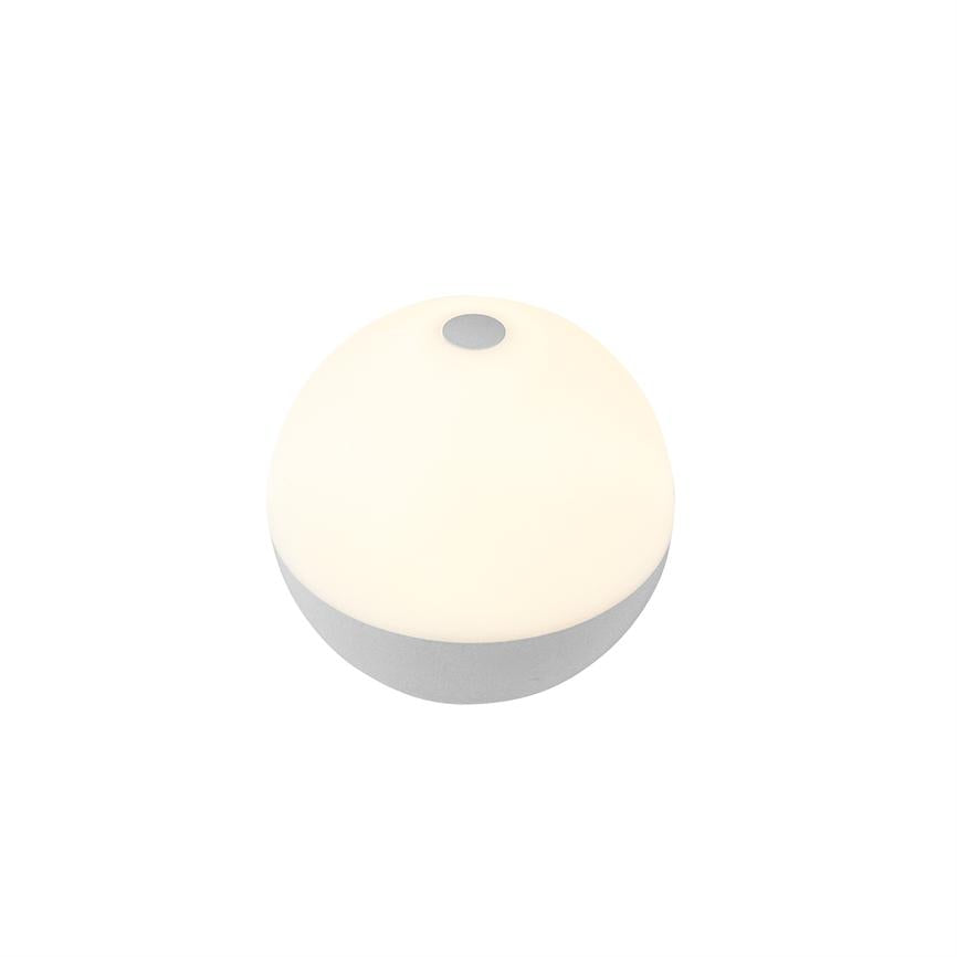 Rund bordlampe med halvkugleformet top, der udsender blødt, varmt lys, og med en lille cirkulær kontakt øverst; står isoleret på en ensartet hvid baggrund med lav grå bund.