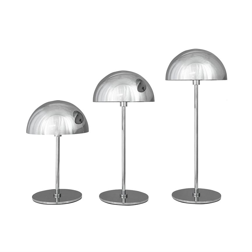 Tre krom bordlamper står i række i stigende højde; halvklodeformede skærme og slanke søjler reflekterer lys mod en neutral hvid baggrund.