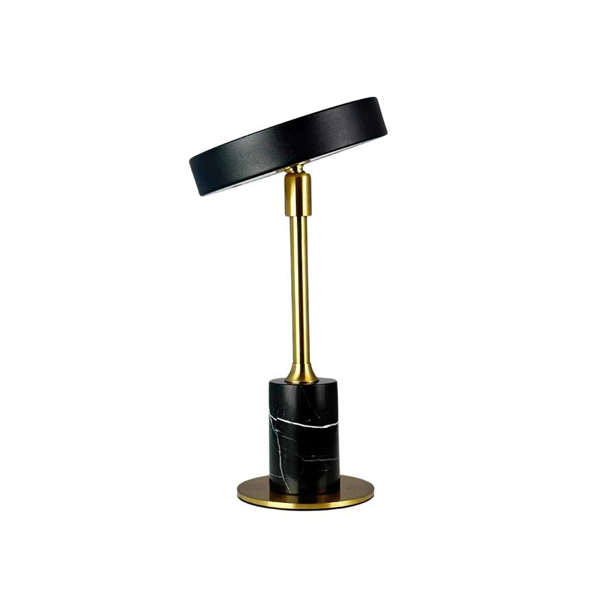 Bordlampe med sort, let tiltet skærm, guldfarvet stang og cylindrisk sort marmorbase med hvide årer, placeret på rund guldfarvet fod mod hvid baggrund.