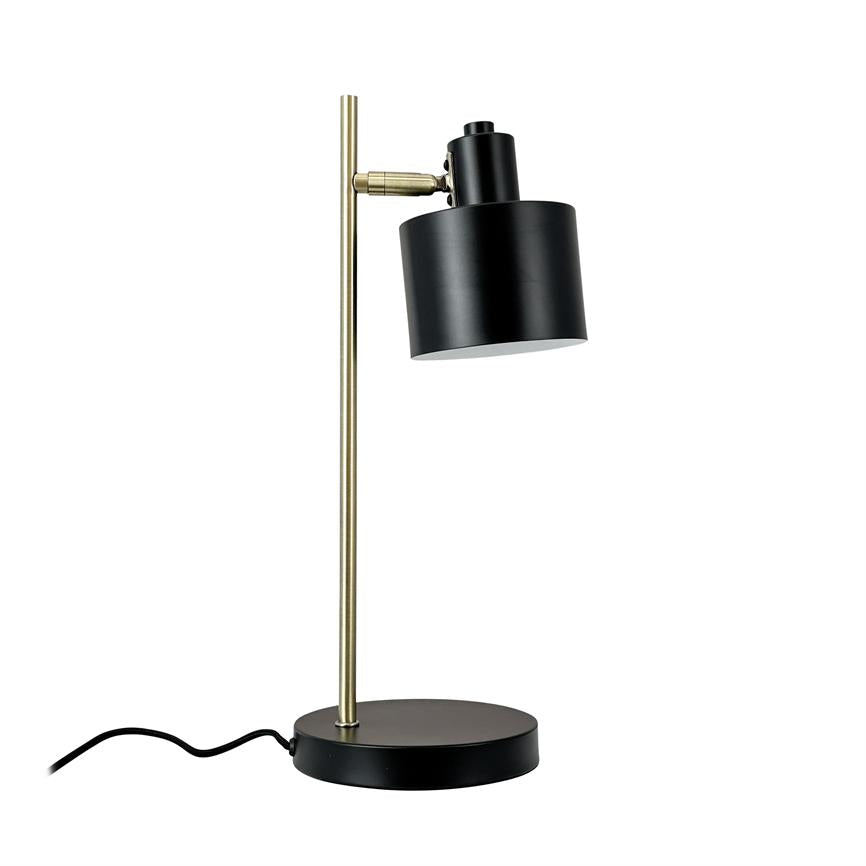 Bordlampe med sort cylindrisk skærm, vippet nedad, monteret på en slank messingstang og rund sort base; synlig sort ledning på ensartet hvid baggrund.